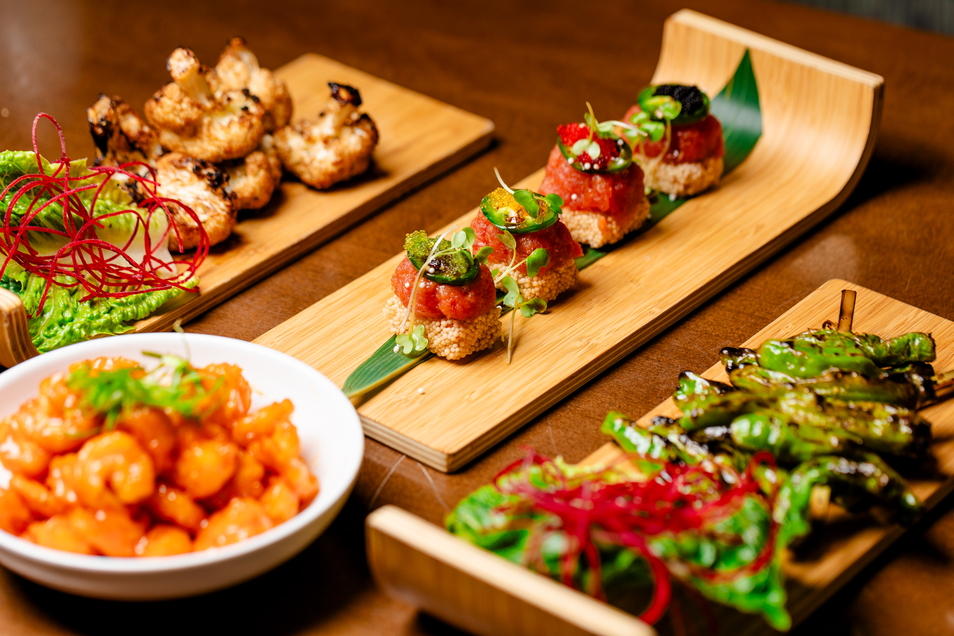 An assortment of small plates with shrimp, grilled vegetables and topped sushi bites on wooden boards